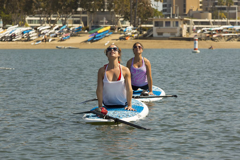 Alumni members practice yoga on paddle boards in Marina del Rey